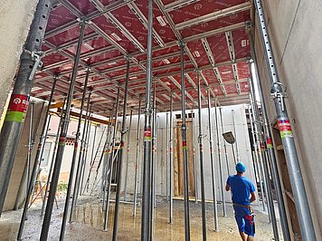 Gradbišče Večstanovanjskega objekta DC208 Stropni opažni sistem RINGER AluDEK z rdečimi opažnimi ploščami in kovinskimi podpornimi spojkami v objektu DC208.